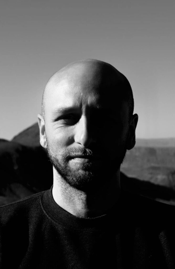 Black and White portrait the author, bald with a beard, approx. 40 years old. Exterior with hills in bkgrd.