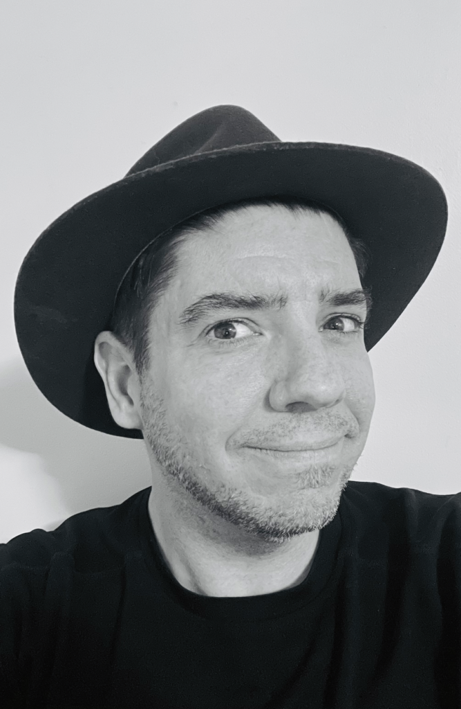 Black and white headshot of the author wearing a black fedora and black shirt