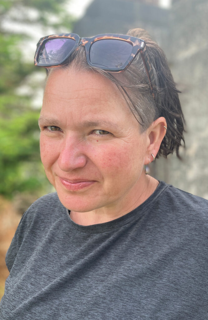 smiling portrait in nature with sunglasses on head wearing a grey t-shirt